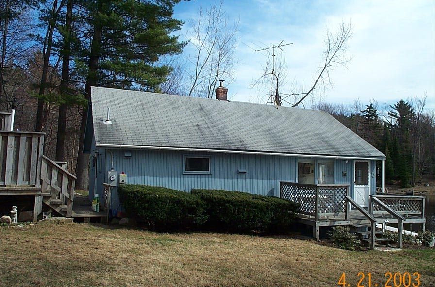 Small blue house with gray roof and wooden porch in a wooded yard