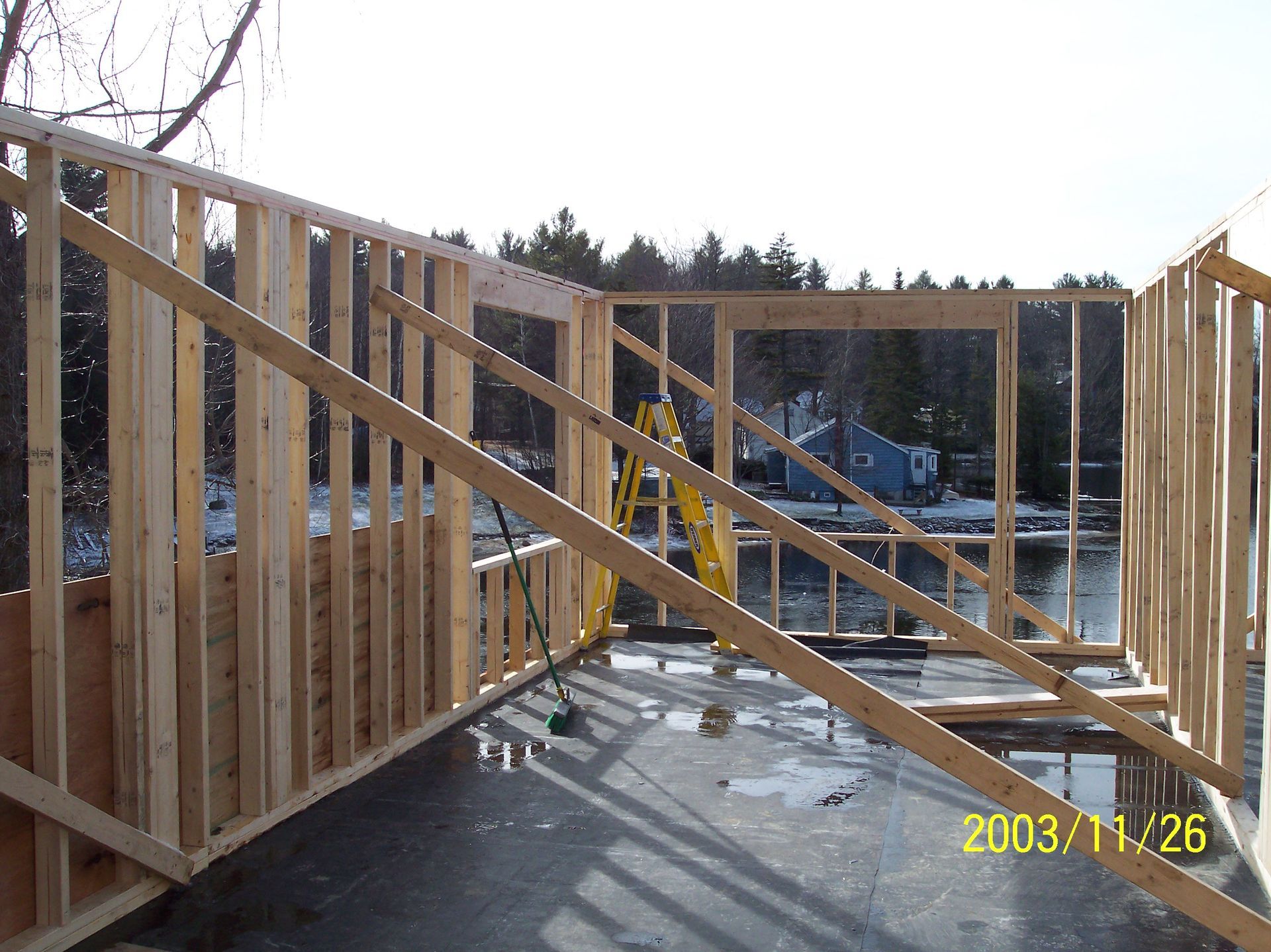 Wood-framed house under construction with diagonal bracing and plywood sheathing on a concrete slab