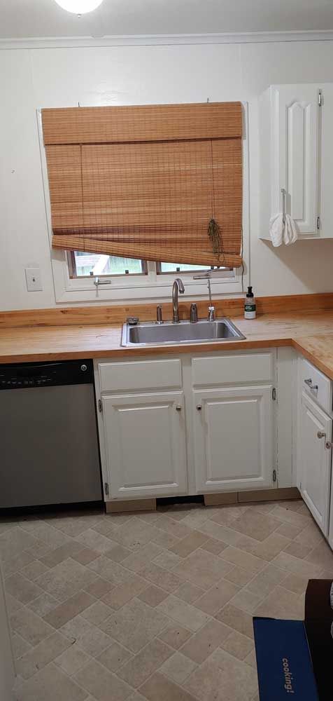 Small kitchen with white cabinets, wooden countertop, sink, and a window with woven blinds.