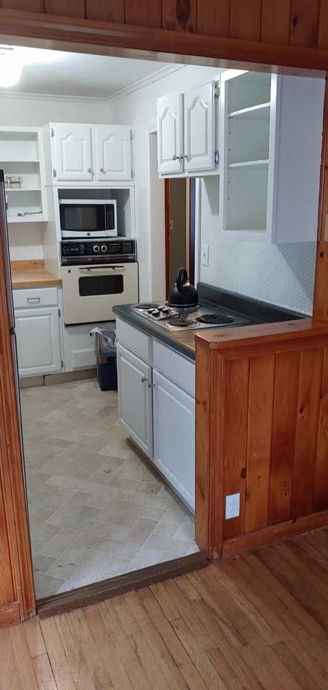 Narrow white kitchen with wood trim, white cabinets, and black countertop viewed through a doorway