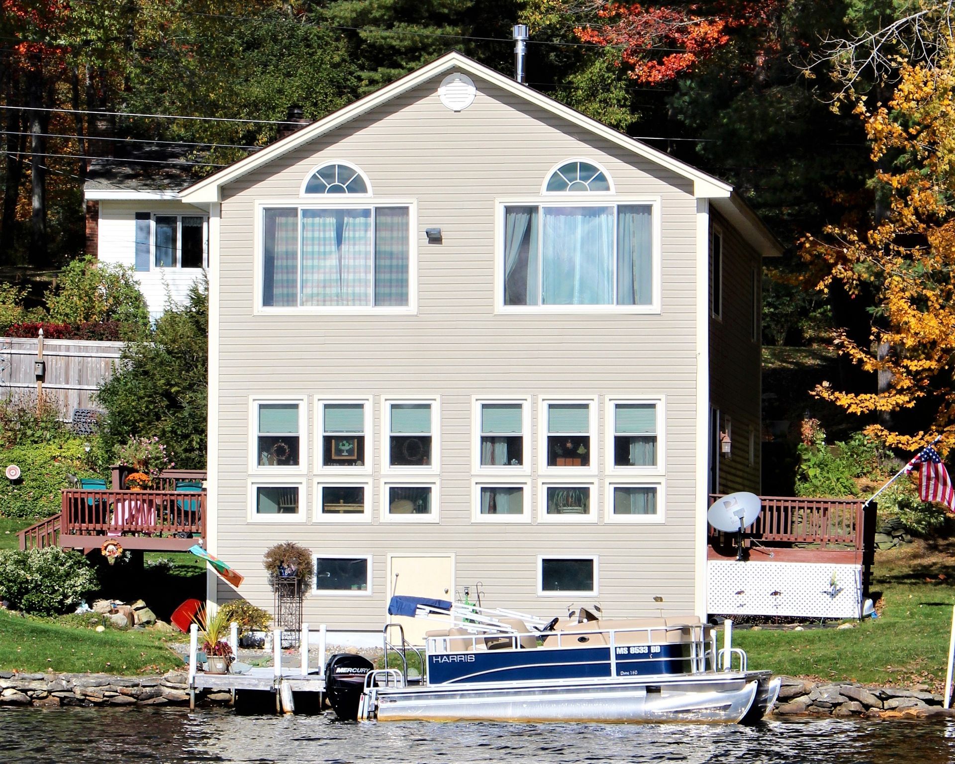 Lakeside house with large windows and a boat docked in front, surrounded by autumn trees