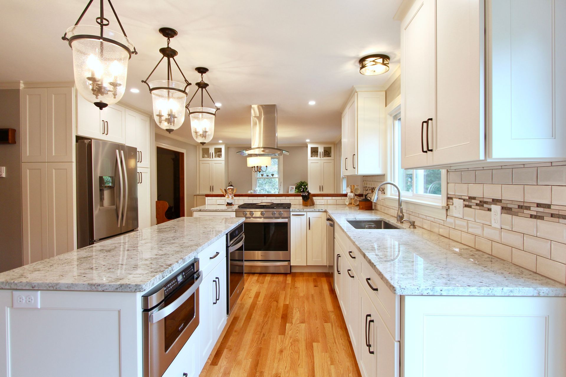 Bright modern kitchen with white cabinets, marble countertops, wood floor, and pendant lights