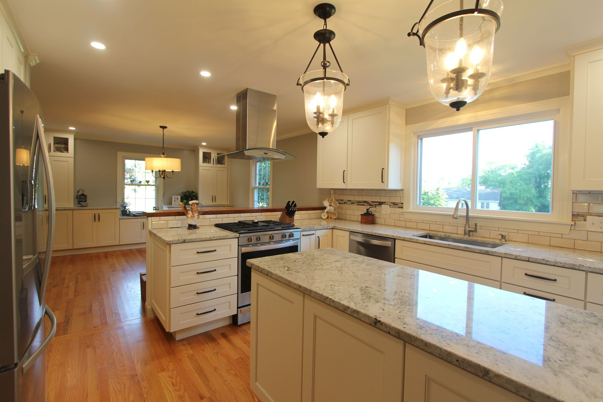 Bright kitchen with white cabinets, granite island, hardwood floors, and large window lights