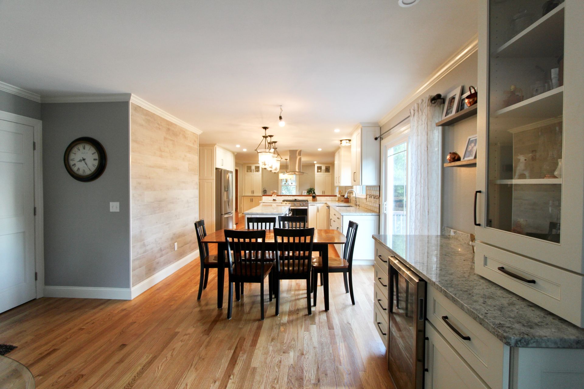 Bright dining room with wooden table, dark chairs, hardwood floors, and open kitchen in the background