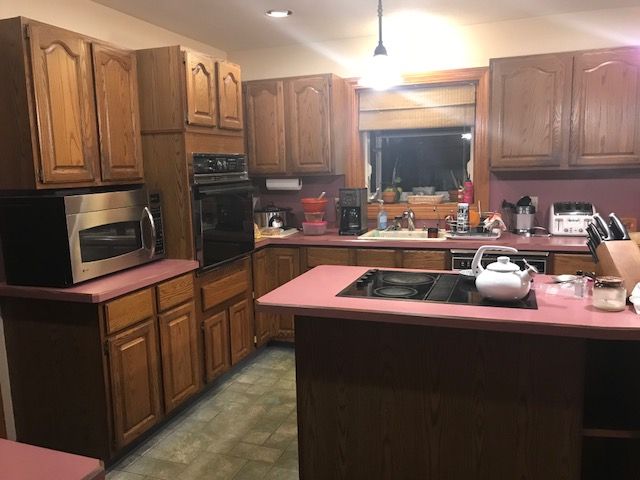 Warm kitchen with wooden cabinets, pink countertops, and a central island under bright ceiling lights