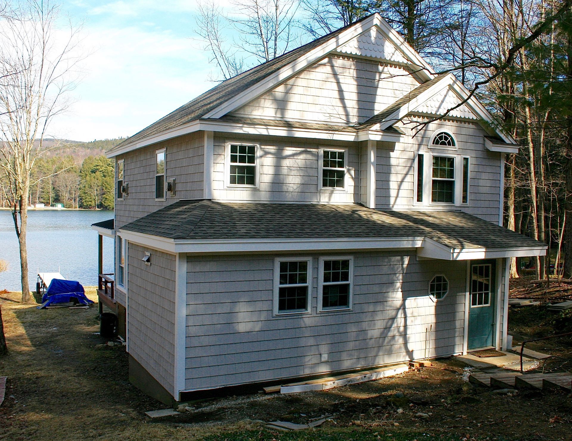 Two-story white house by a lake with trees and a blue boat nearby