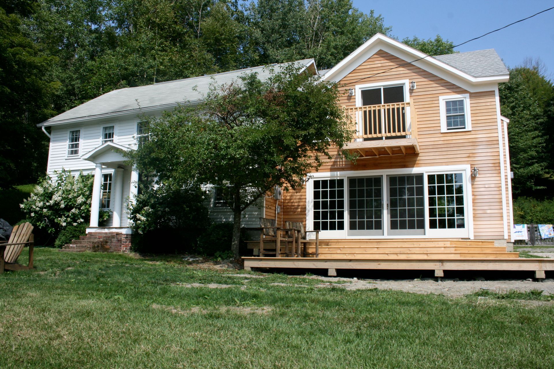 Two-story house with white siding and orange shingle siding, front porch, and large windows in a grassy yard.
