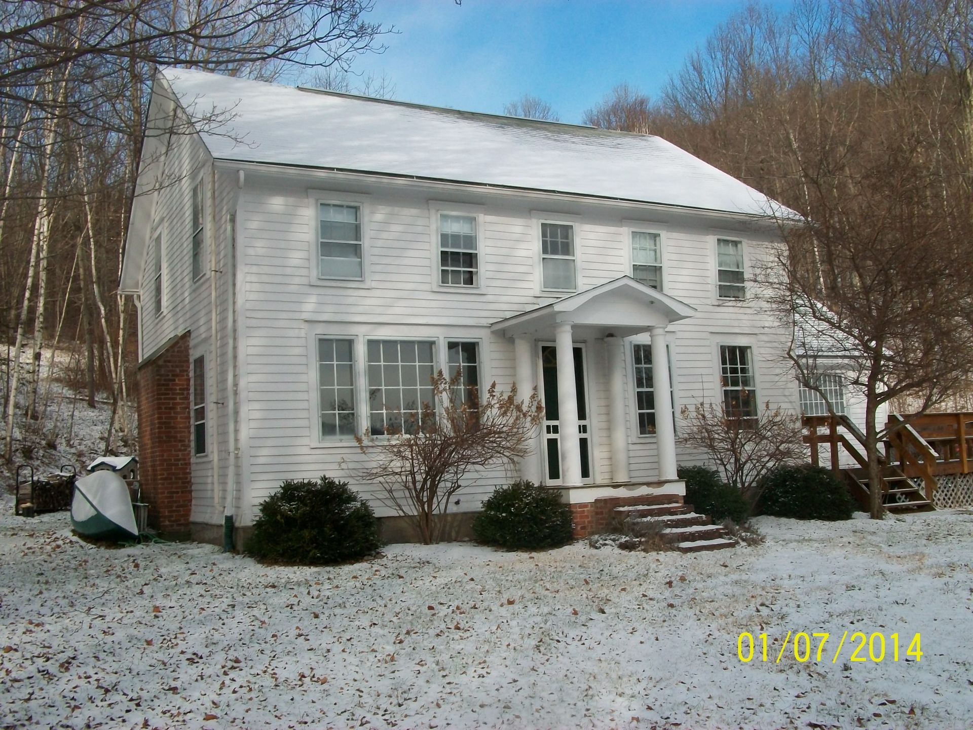 Snow-covered white two-story house with a small front porch and bare trees in winter