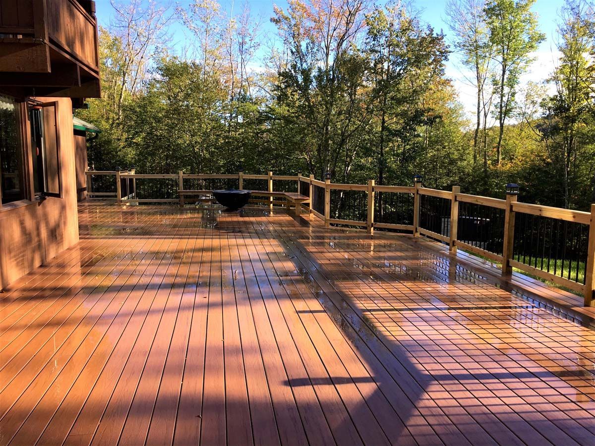 Sunlit wooden deck with railing beside a house, bordered by trees in autumn light