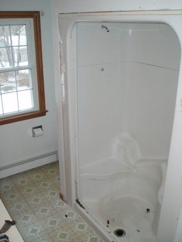 Small bathroom with an unfinished white shower stall next to a window.