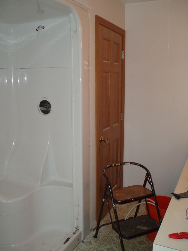 Bathroom with white shower stall, wooden door, and a black chair beside a red bin.