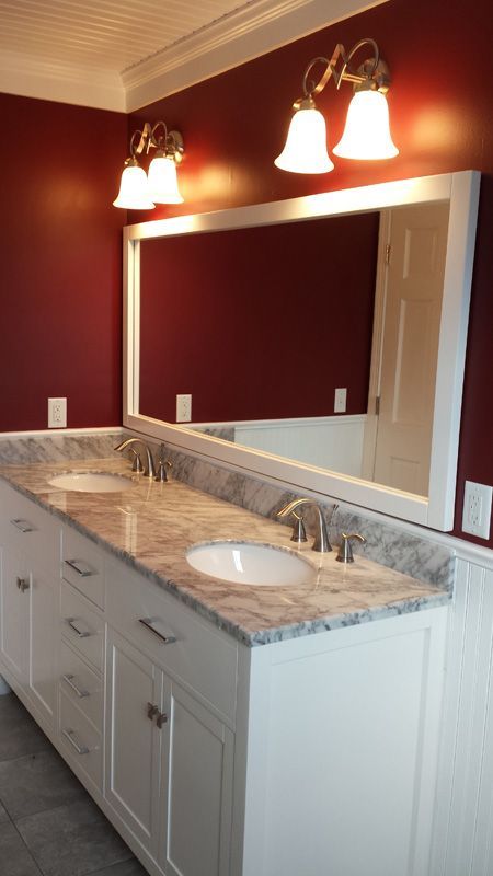 Bathroom vanity with double sinks, marble countertop, large mirror, and warm wall sconces in a red room