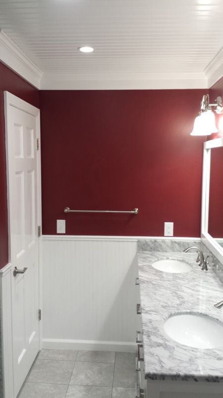 Bathroom with red walls, white wainscoting, granite vanity, mirror lights, and towel bar.