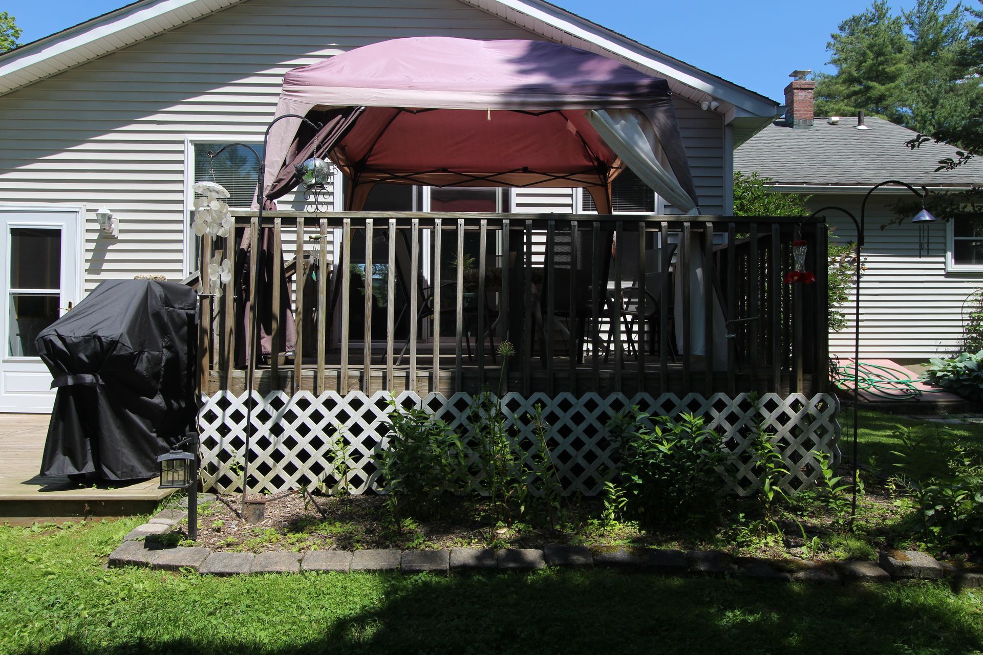 Backyard deck with black railing, pink canopy, and grill beside a beige house