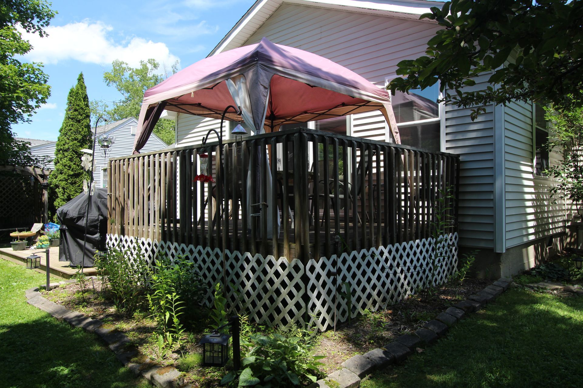 Backyard deck with wooden railing, pink patio umbrella, and a house beside a grassy yard
