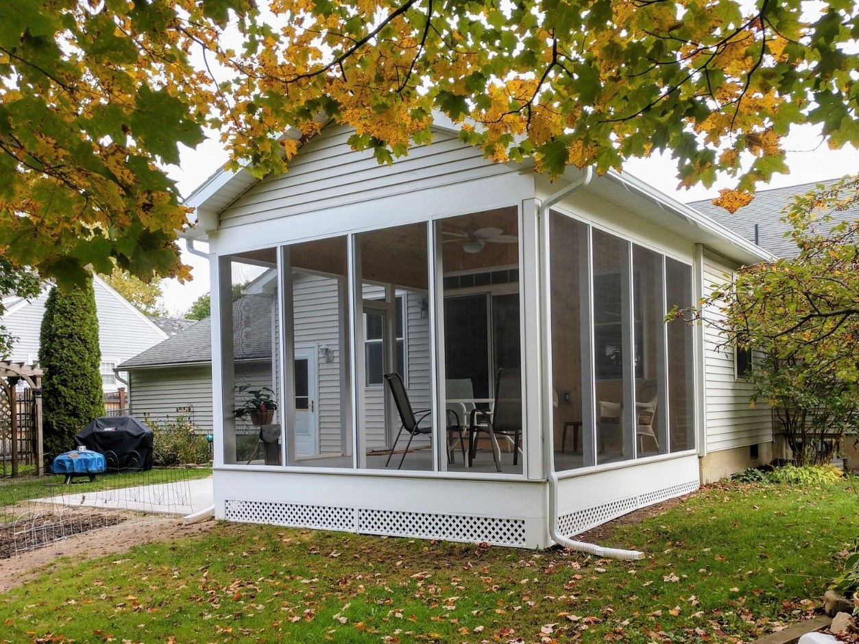 Screened porch on a house, with white trim and autumn leaves overhead.