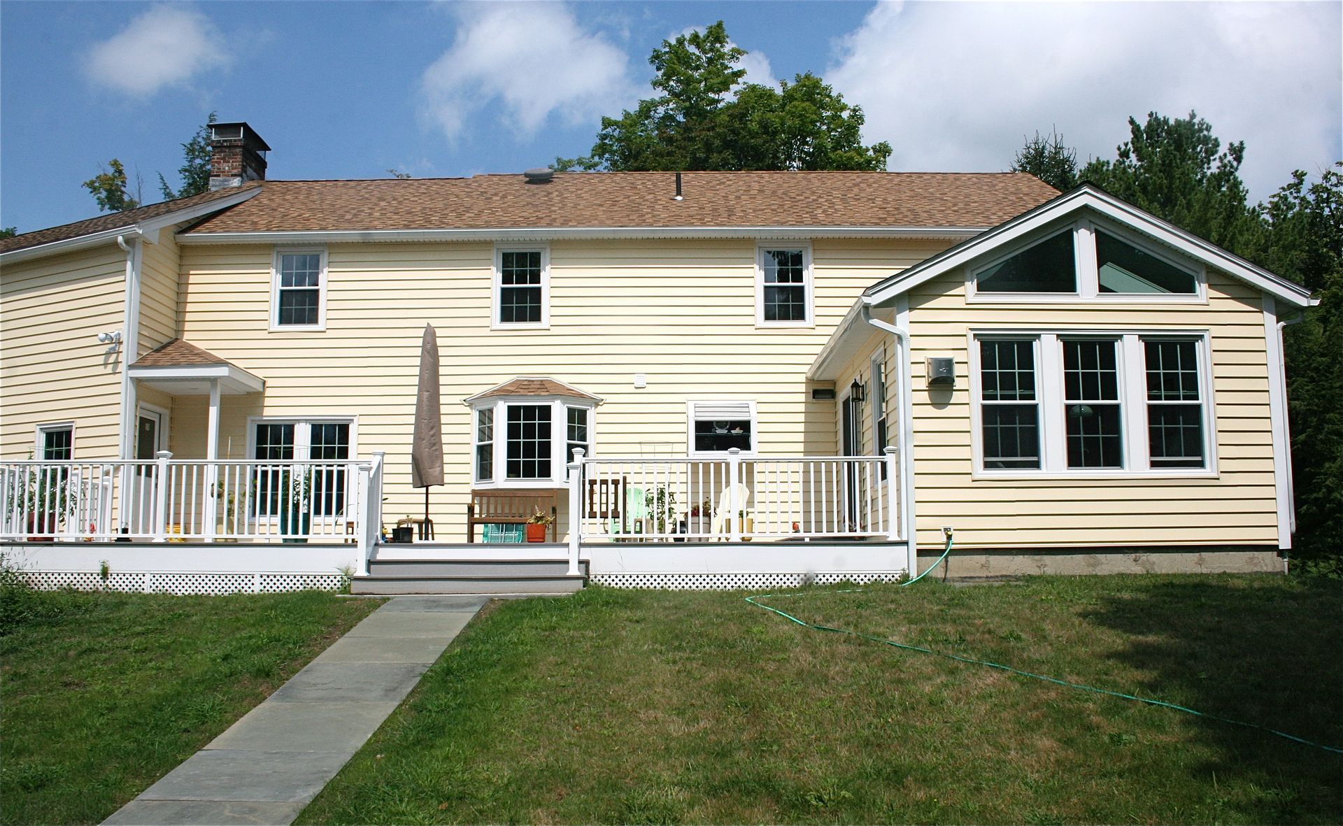 Cream-colored house with front porch, white railing, and a grassy yard under a partly cloudy sky