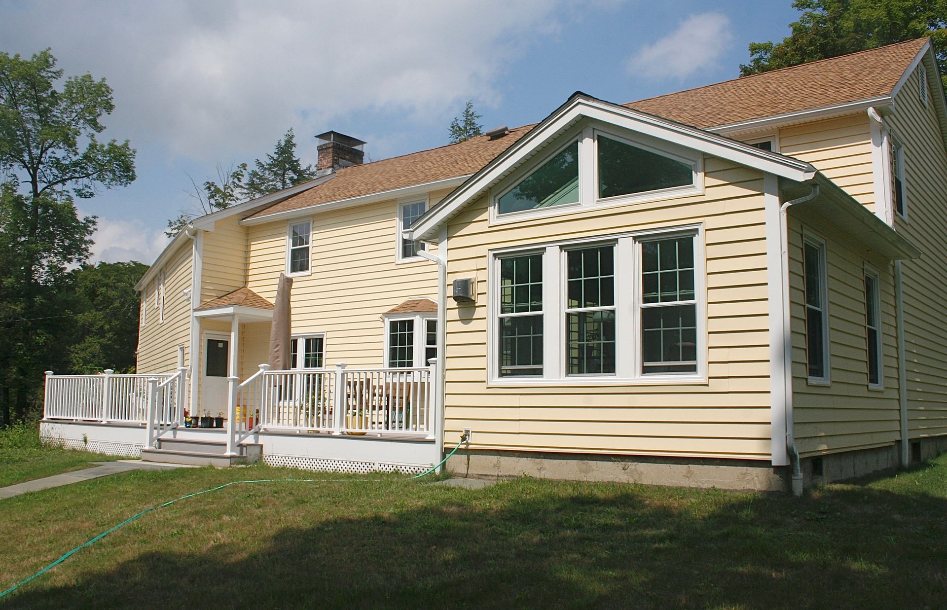 Yellow house with white trim, porch, and large windows under a blue sky