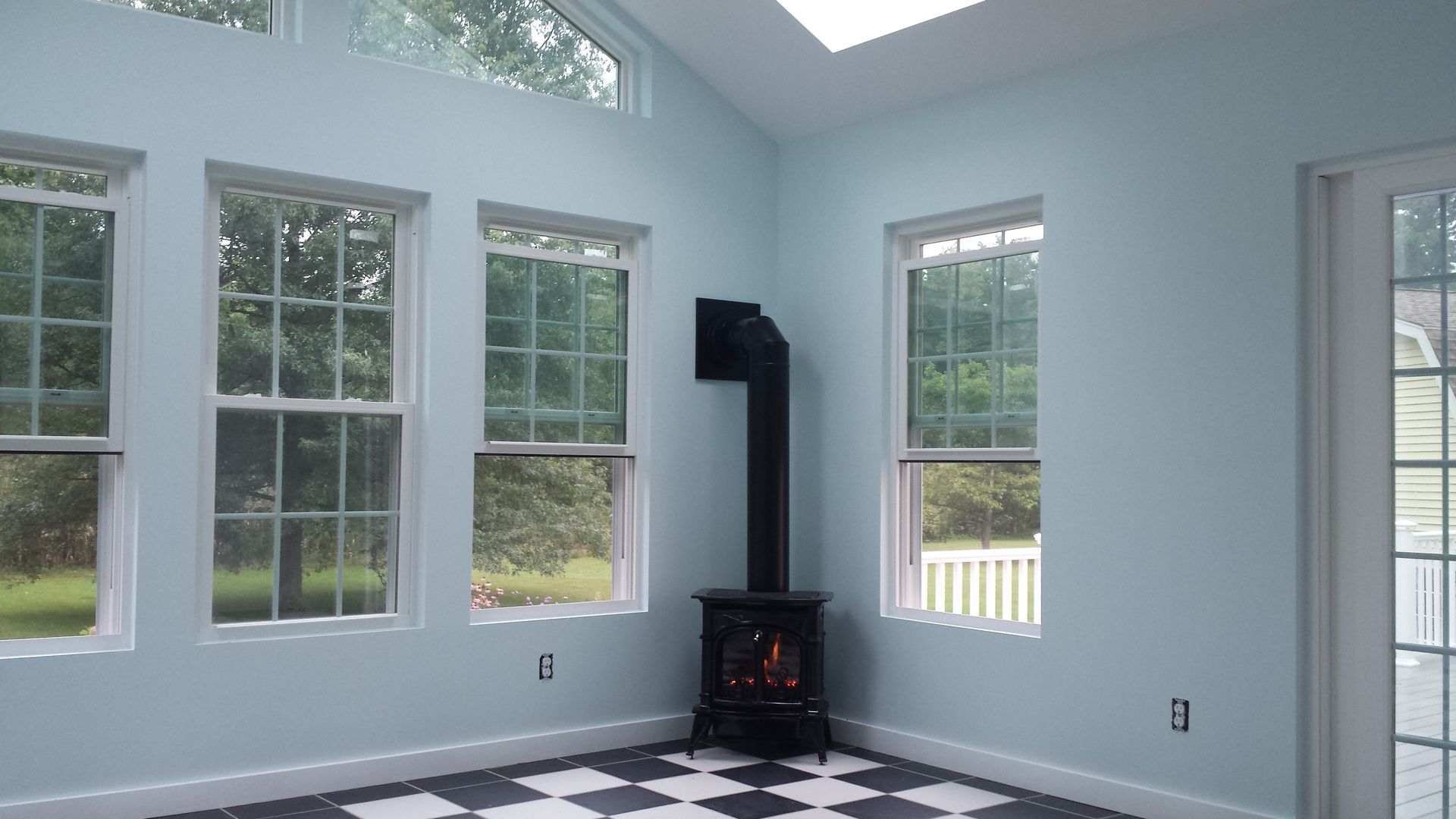 Bright room with large windows, white walls, black wood stove, and checkered black-and-white floor