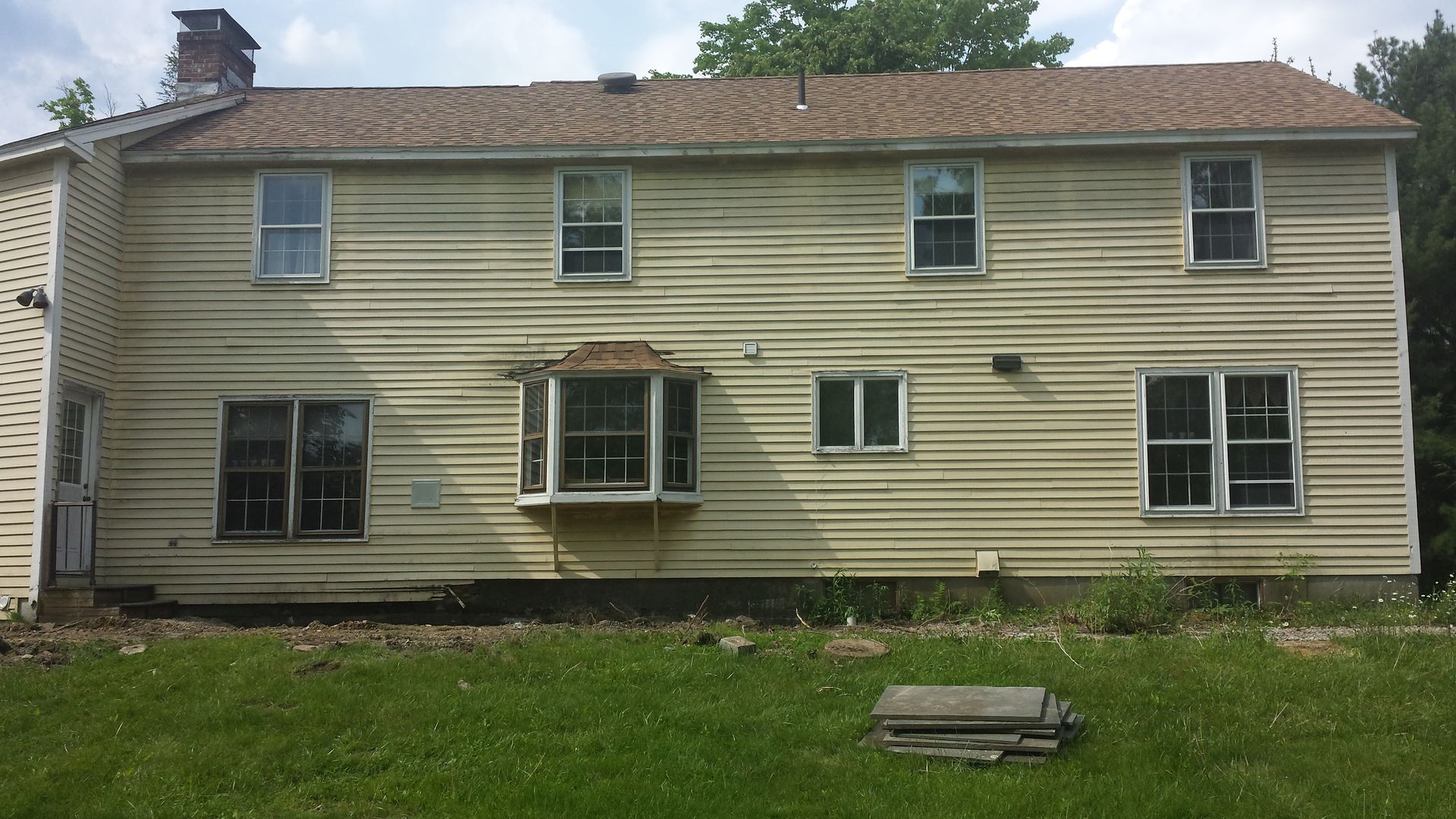 Two-story beige house with white trim, several windows, and a grassy yard under an overcast sky