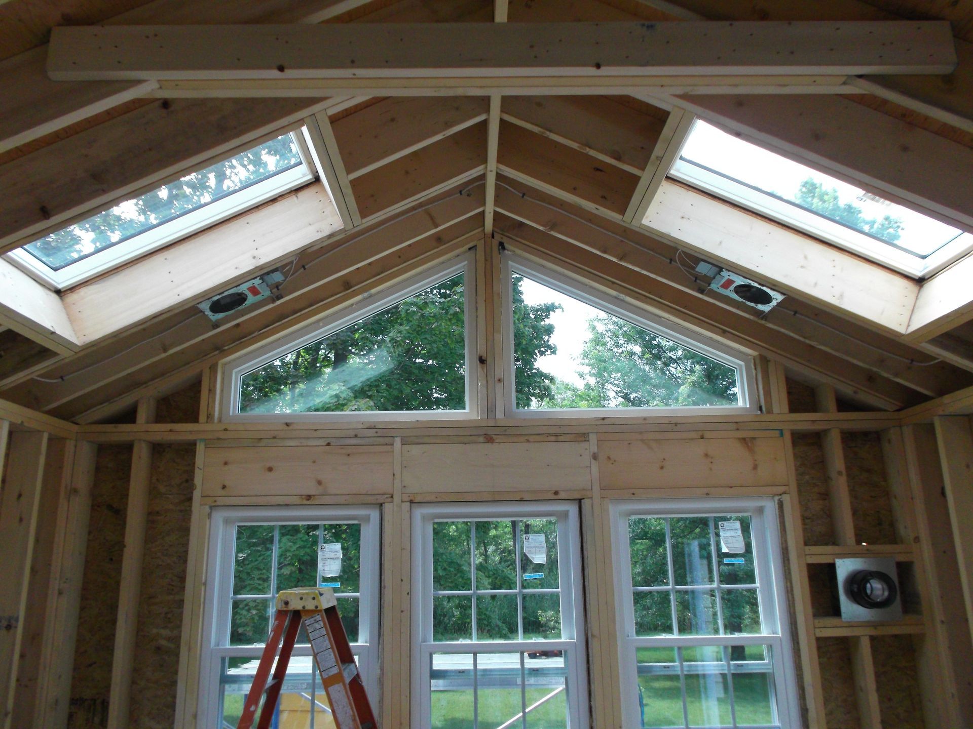 Wooden sunroom interior with skylights, large windows, and a ladder beneath the peaked ceiling.