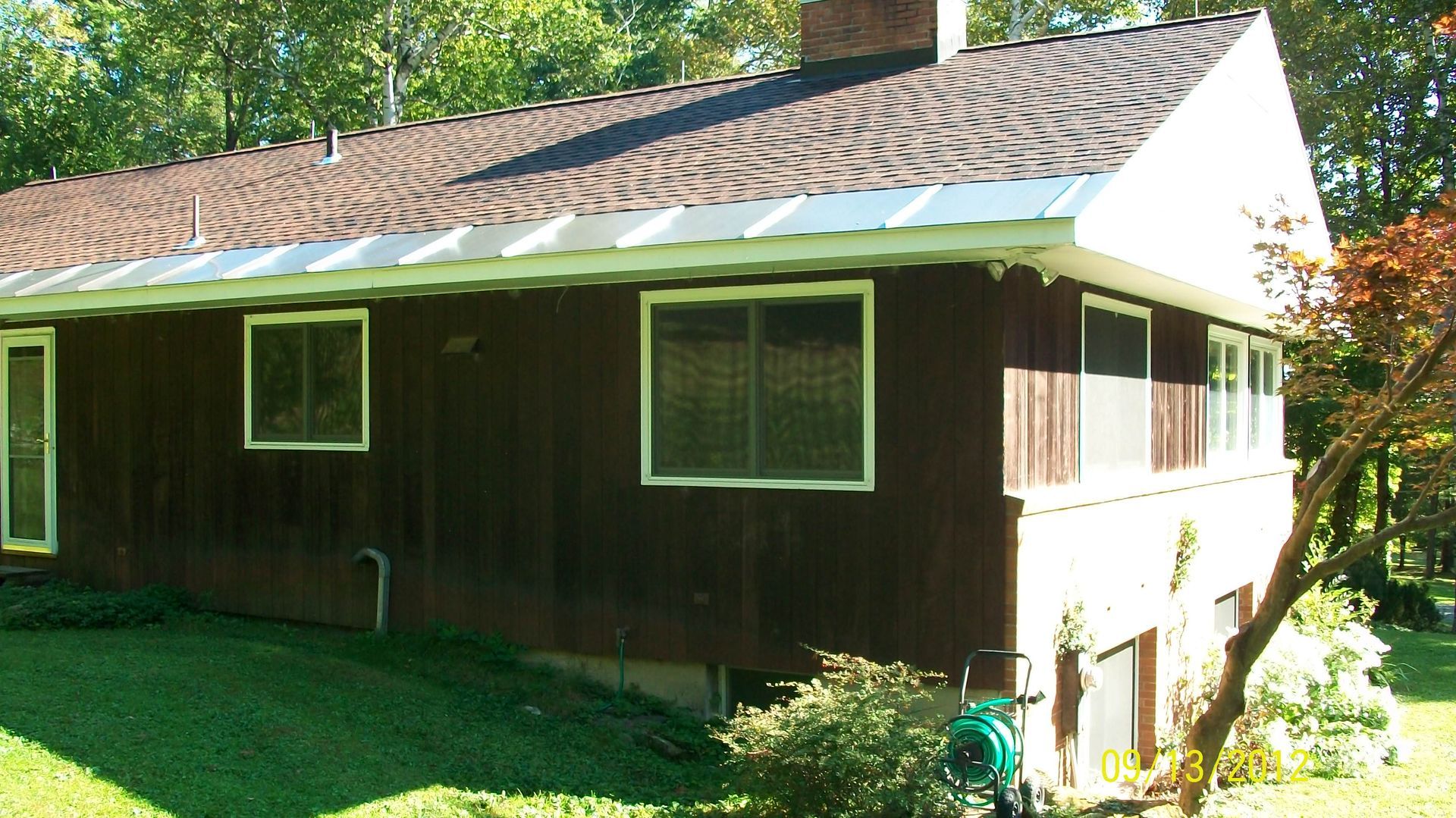 Brown house with white-trimmed windows, a tiled roof, and a grassy yard in bright sunlight