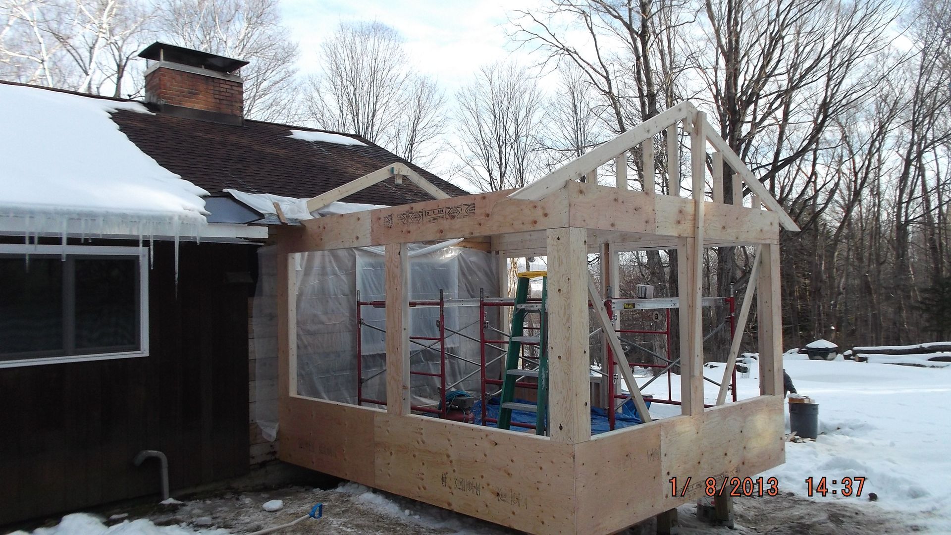 Partially built wooden sunroom addition beside a house in a snowy yard
