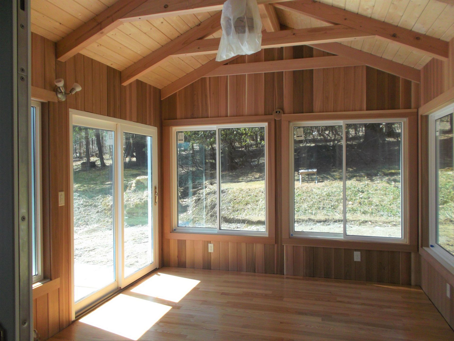 Empty wooden sunroom with large windows and a glass door, showing sunlight on the floor.