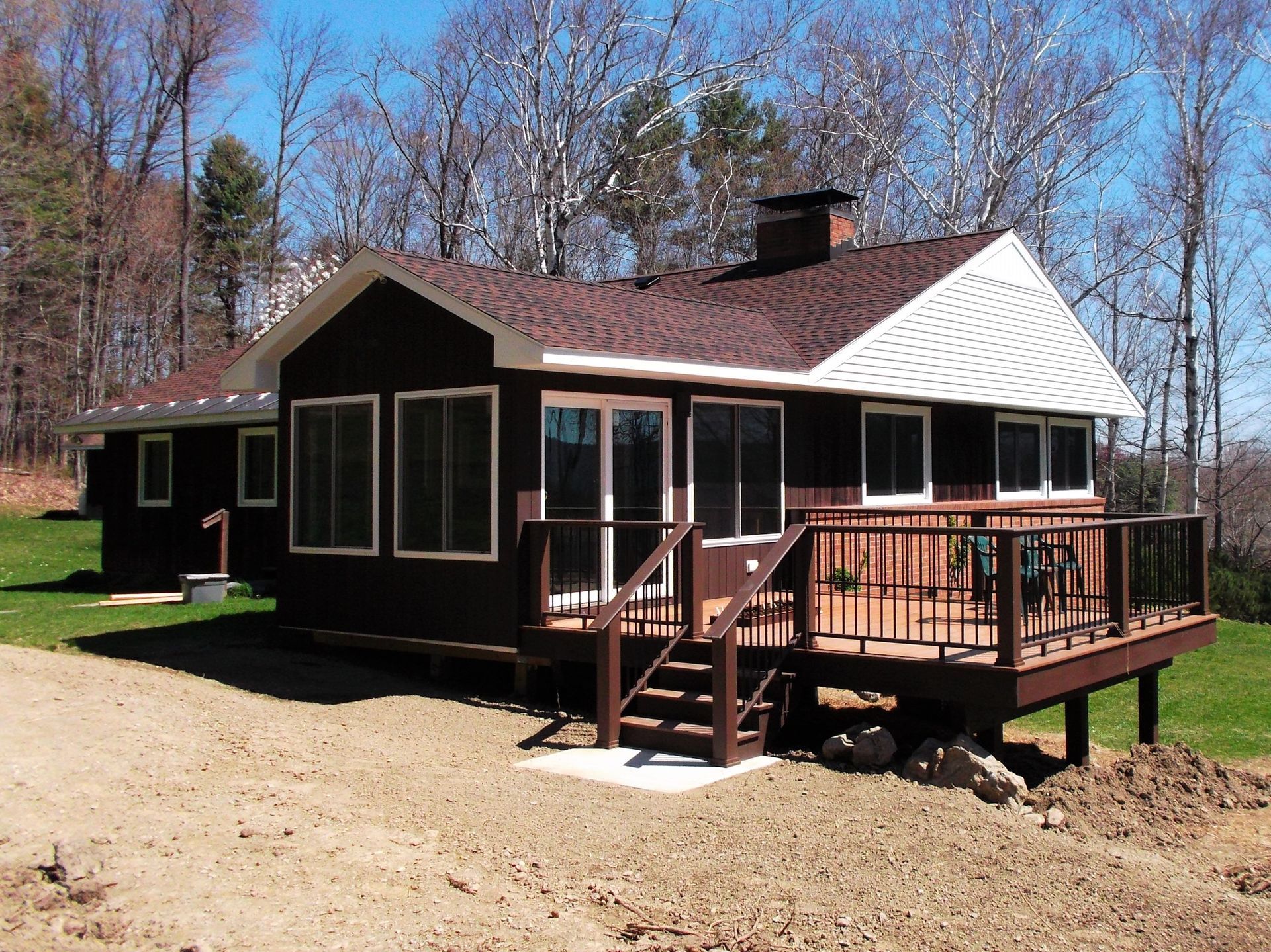 Small dark cabin with white roof and wooden deck in a wooded clearing