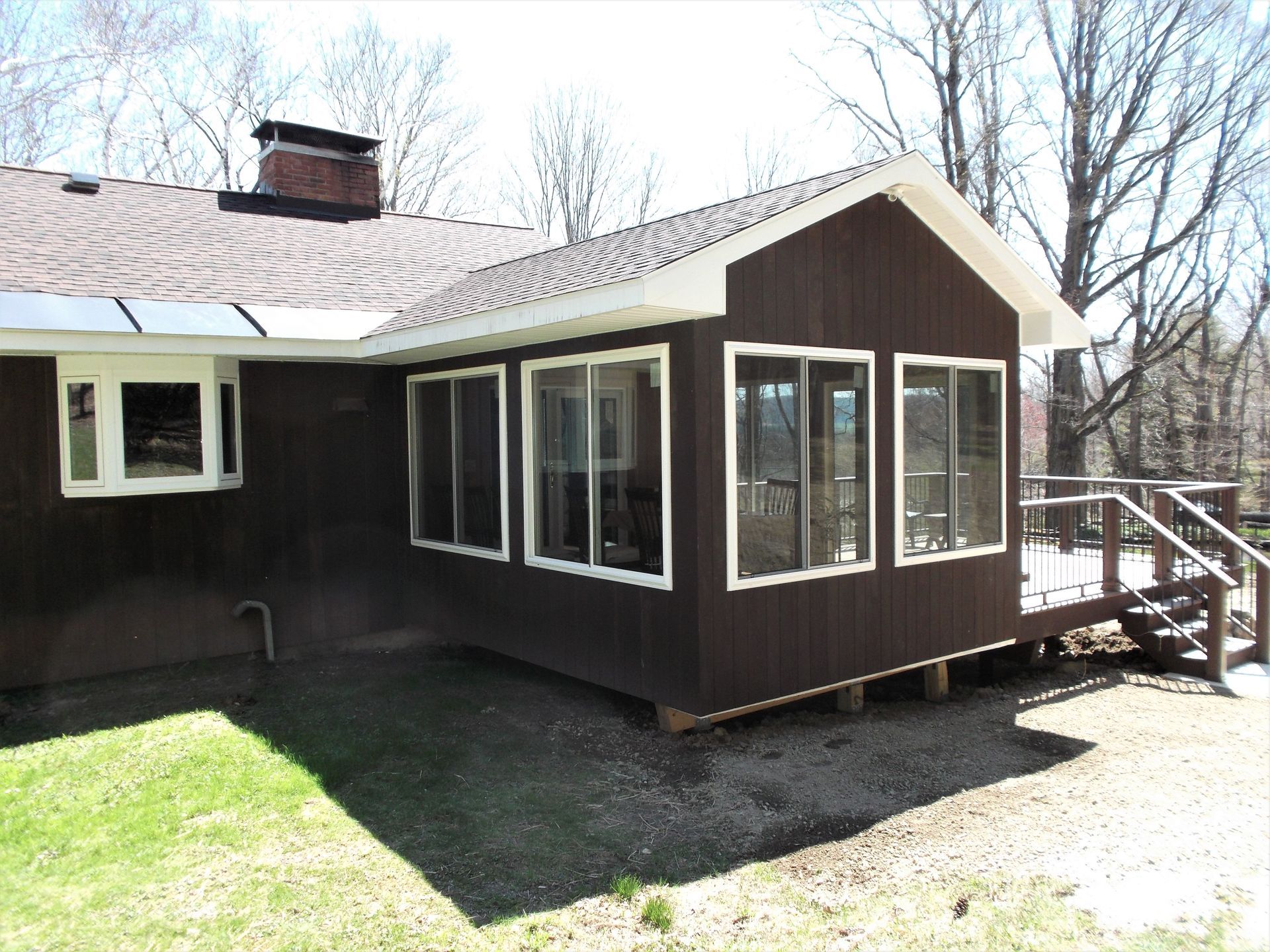 Back of a dark brown house with a screened porch, white-trimmed windows, and a small wooden ramp in a yard