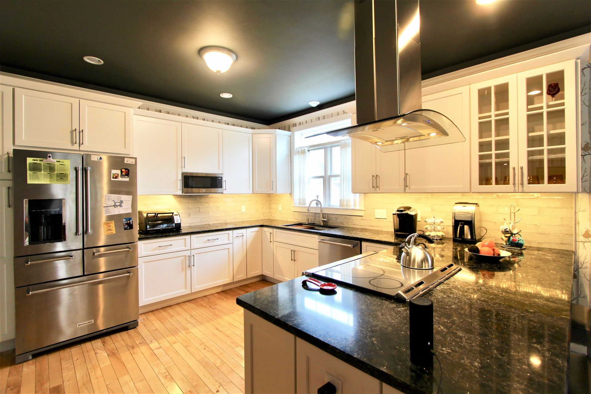 Modern kitchen with stainless steel appliances, white cabinets, island, and black granite countertops