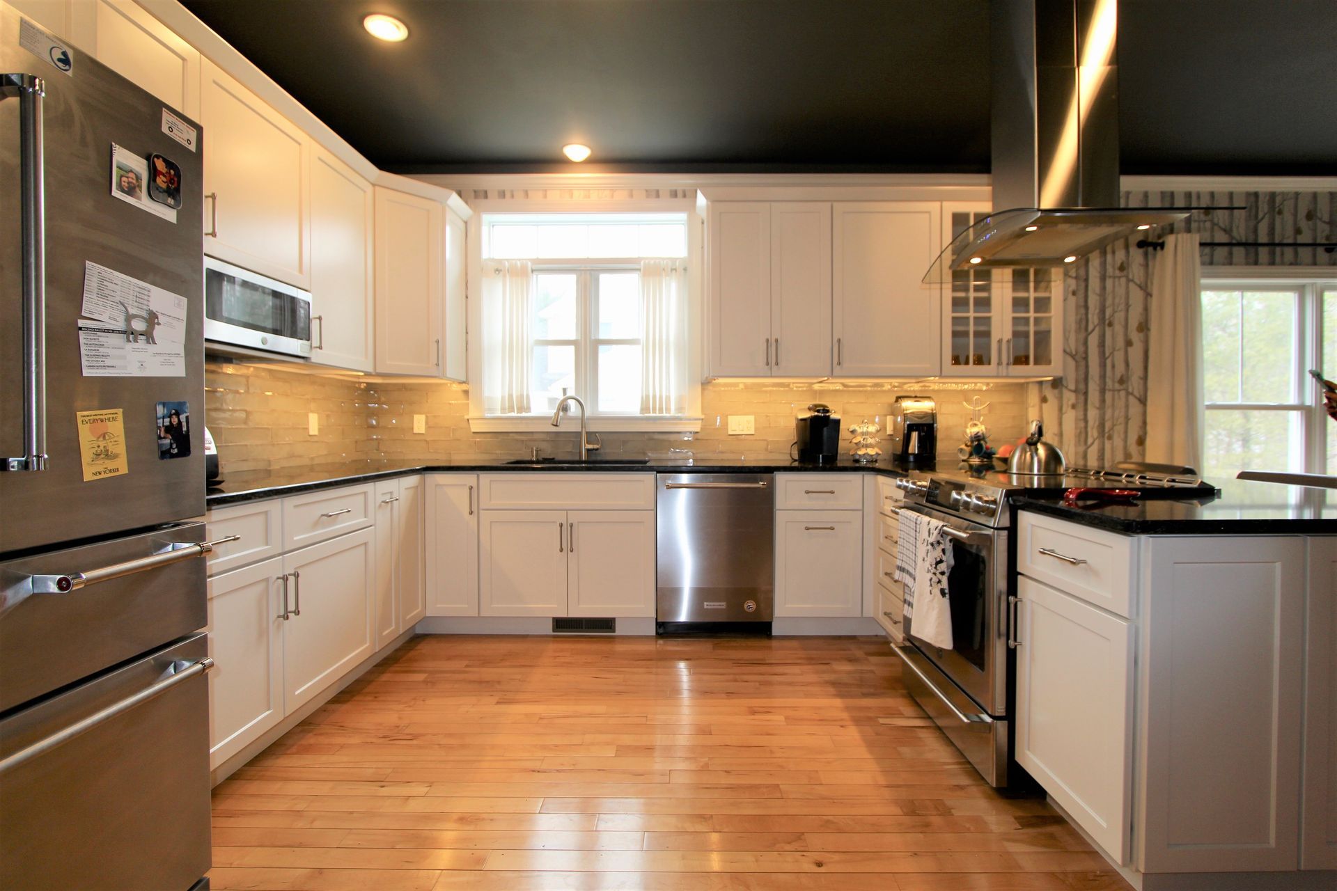Modern kitchen with white cabinets, stainless appliances, wood floor, and black ceiling with recessed lights