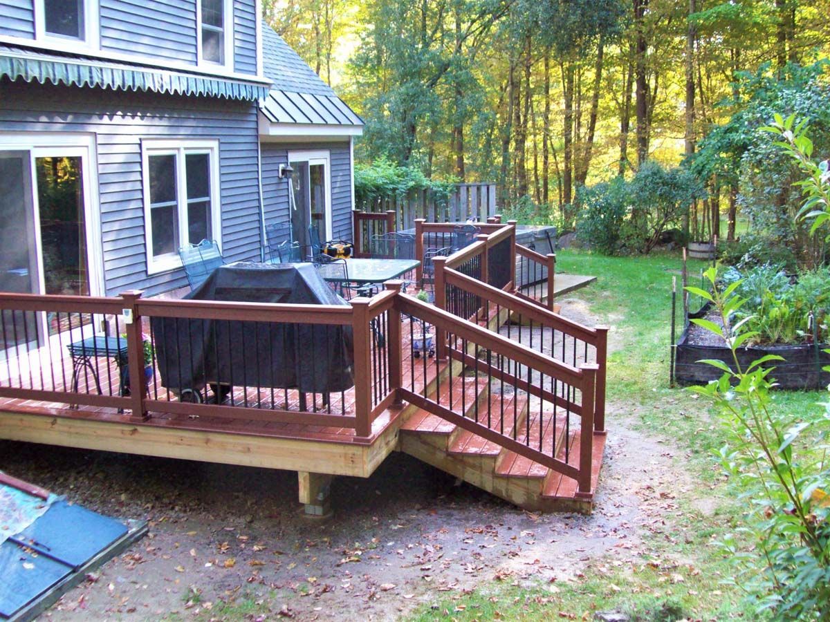 Backyard deck with wooden ramp beside a house, surrounded by trees and garden beds.