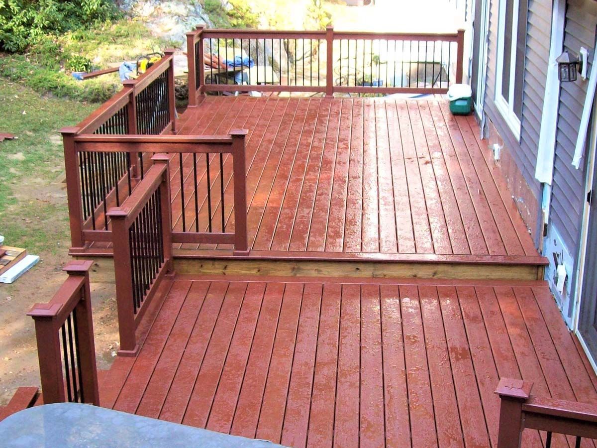 Wooden backyard deck with railings and stairs beside a house, with a wooded yard beyond.
