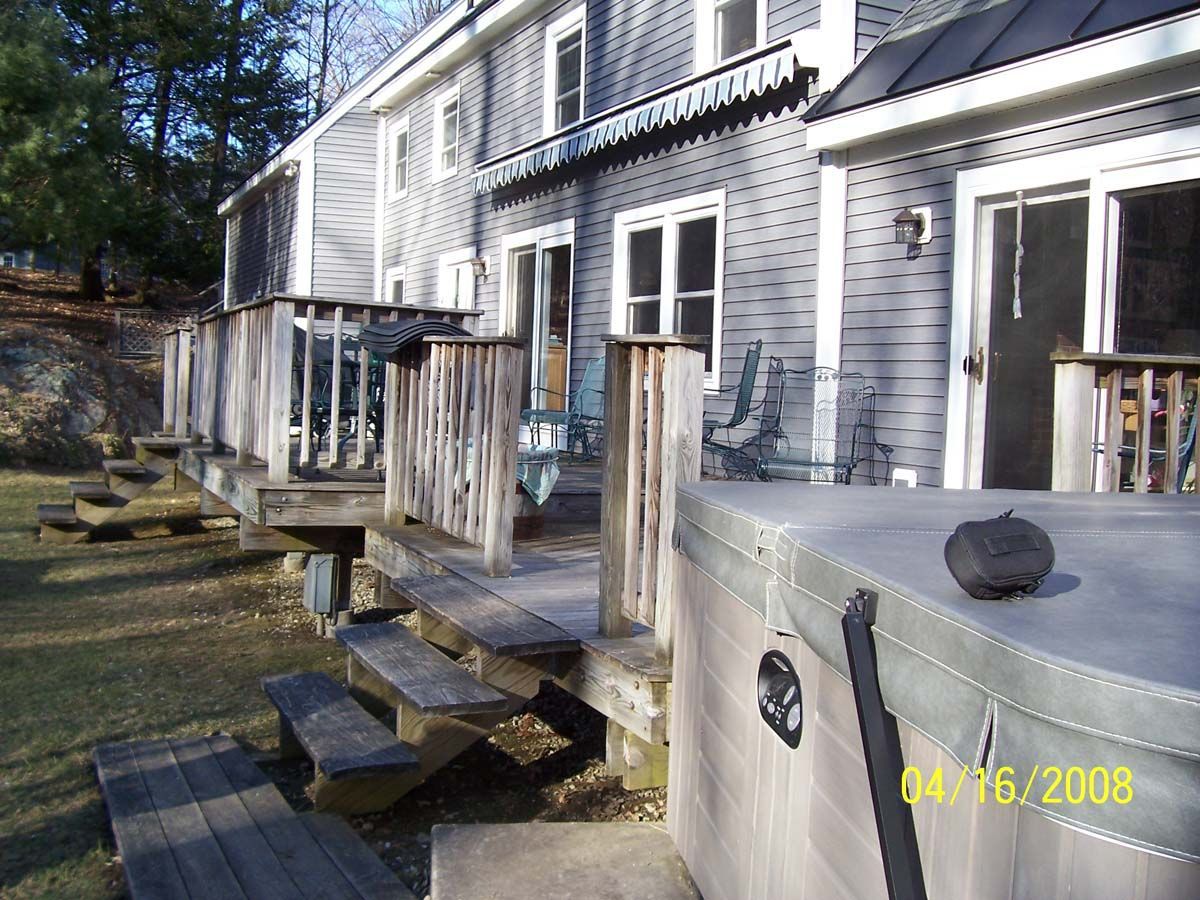 Back porch of gray house with wooden steps and railing, showing a deck and yard in daylight