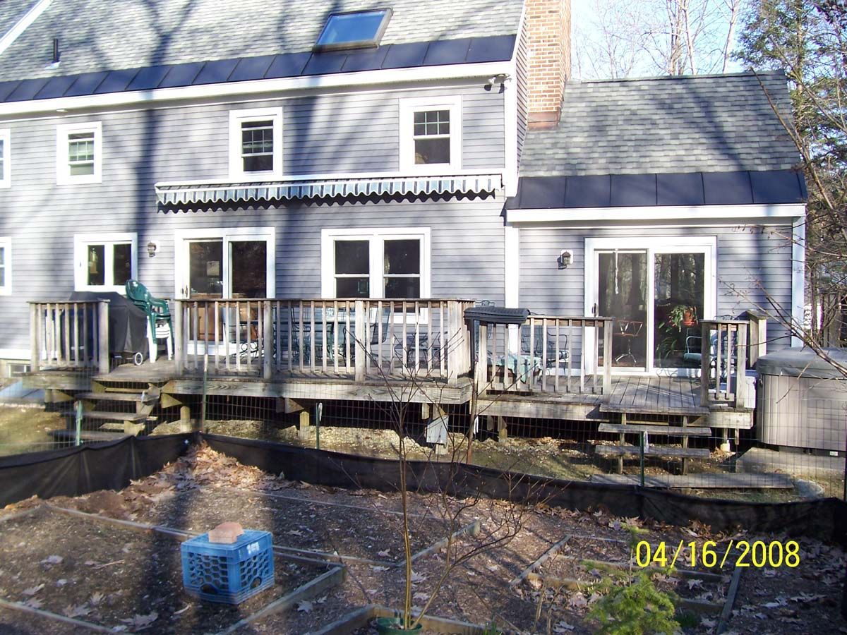 Backyard deck attached to a gray house with white railings and patio doors, viewed in winter.