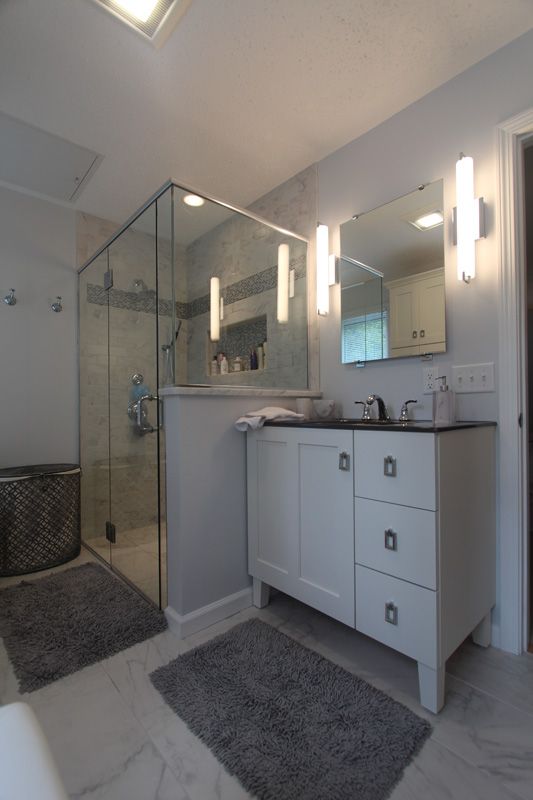 Modern white bathroom with glass shower, vanity, mirror, and gray rugs