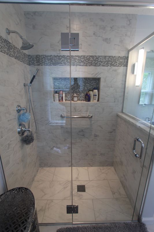 Glass-enclosed walk-in shower with gray tile, built-in shelf, and a small window.