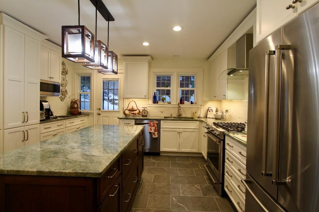Bright modern kitchen with marble island, dark cabinets, stainless fridge, and pendant lights