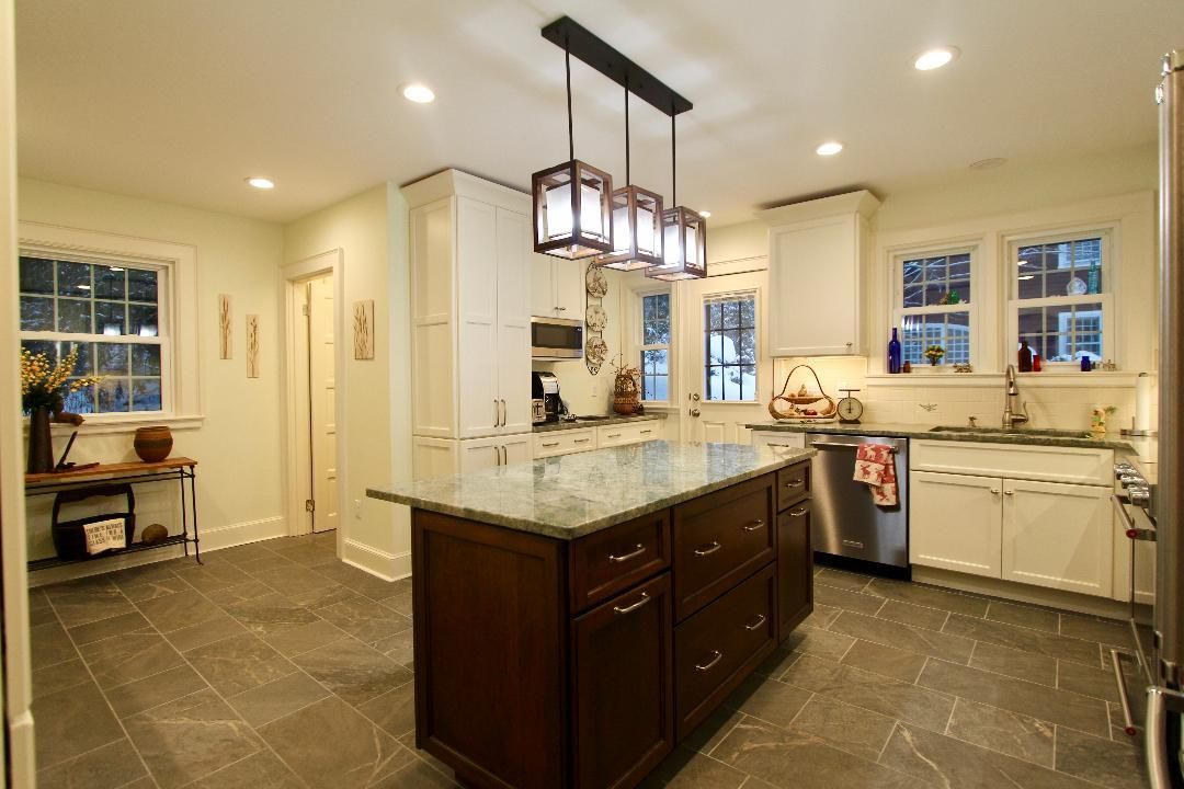 Bright, modern kitchen with a large island, pendant light, white cabinets, and gray tile floor
