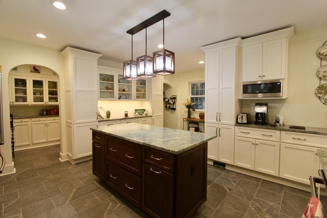Spacious beige kitchen with a dark wood island, marble countertop, and hanging pendant lights