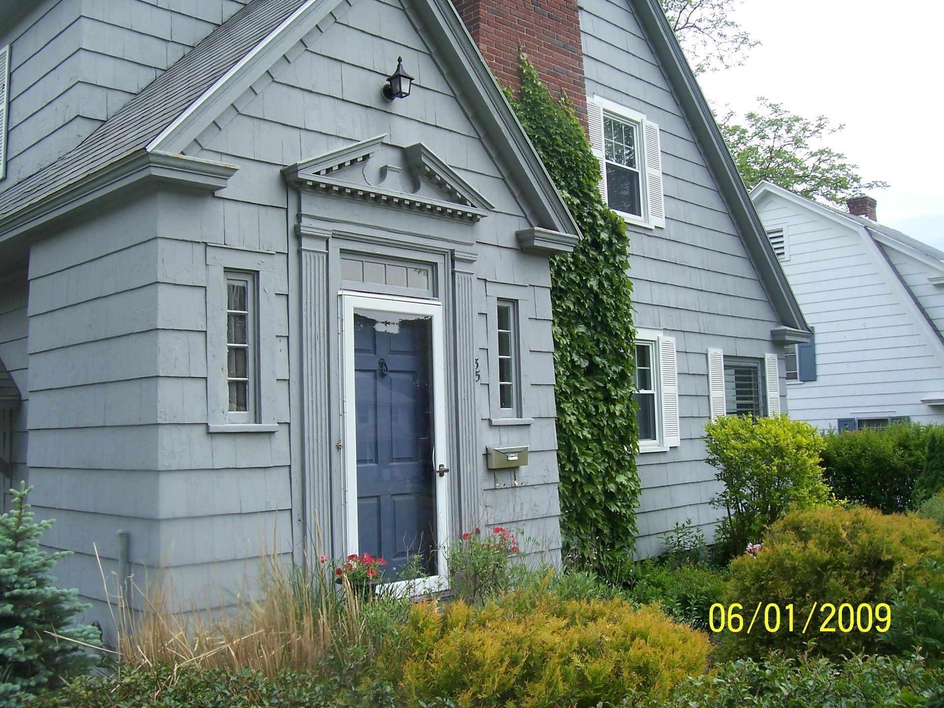 Gray house exterior with blue door, white trim, and ivy climbing the front wall