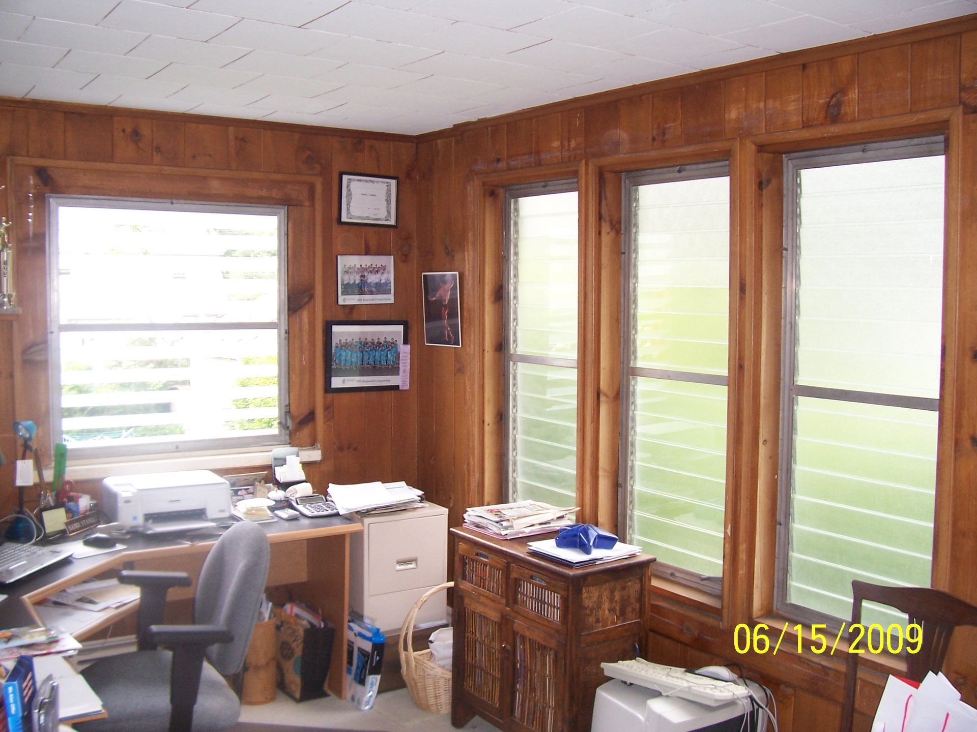Wood-paneled home office with desk, chair, papers, and bright windows with blinds