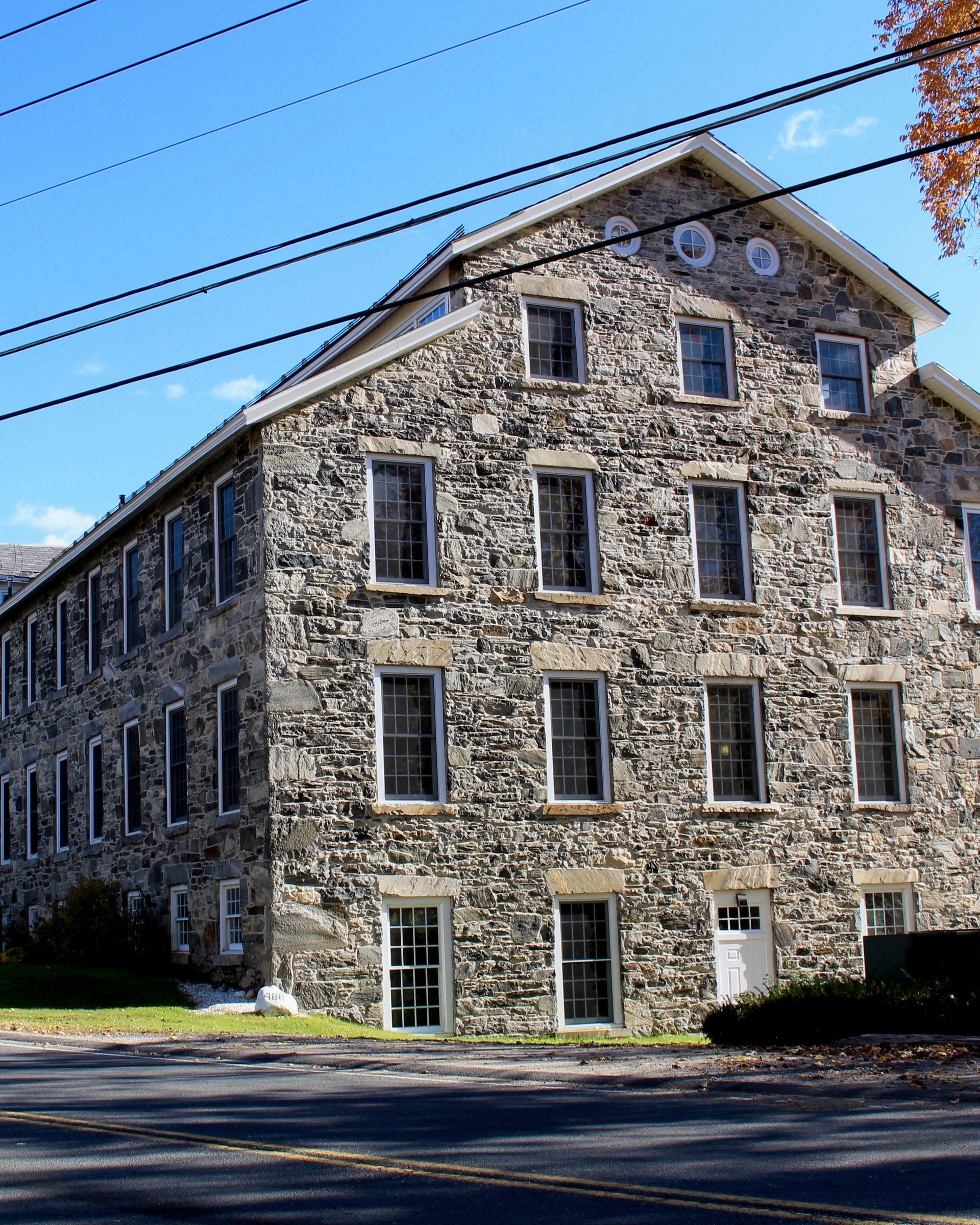 Stone historic building with multiple windows beside a road under a blue sky