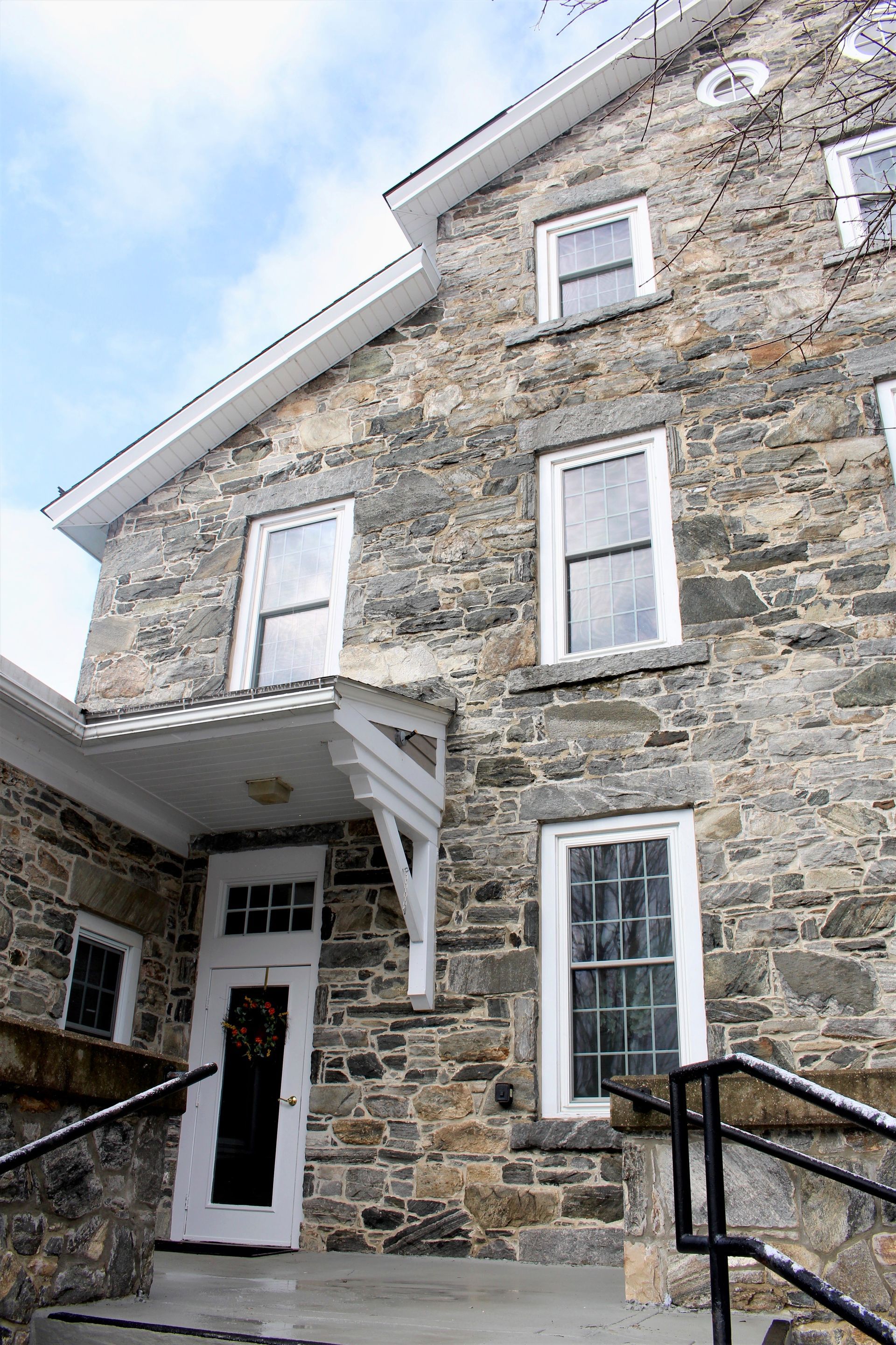 Stone house with white-trimmed windows and a small covered entrance, viewed from below.