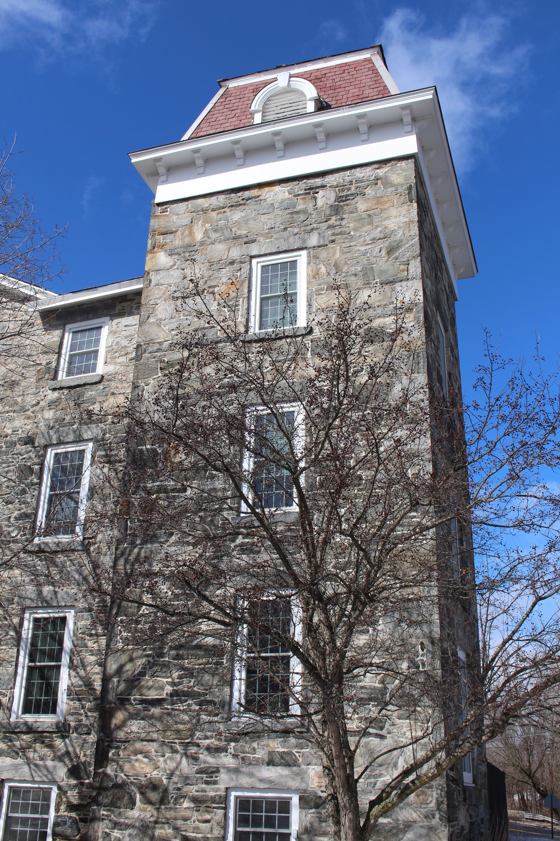 Stone tower building with red roof and bare trees against a blue sky
