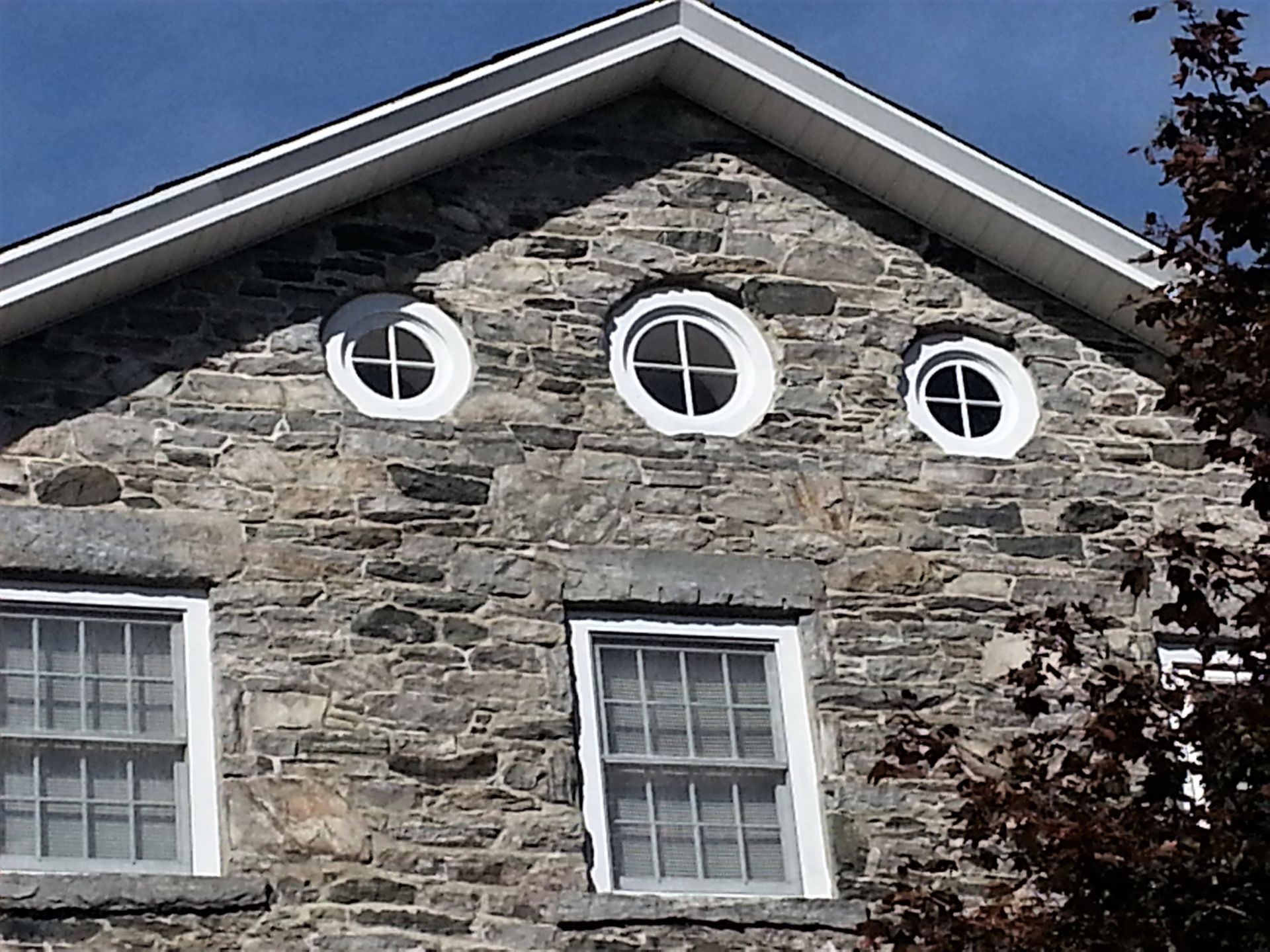 Stone building facade with three round attic windows and two rectangular windows under a blue sky