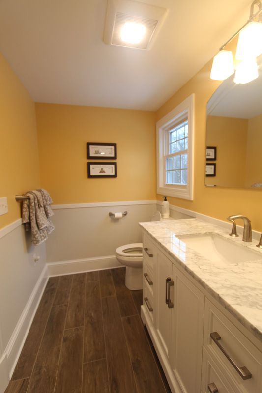 Bright bathroom with yellow walls, white vanity, toilet, and wood-look floor.
