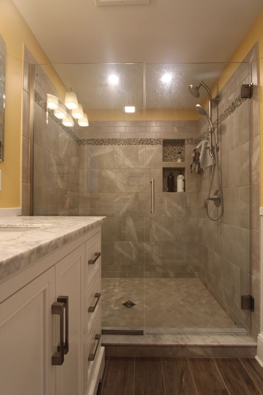 Modern bathroom with glass shower, beige tile, marble countertop, and vanity lights