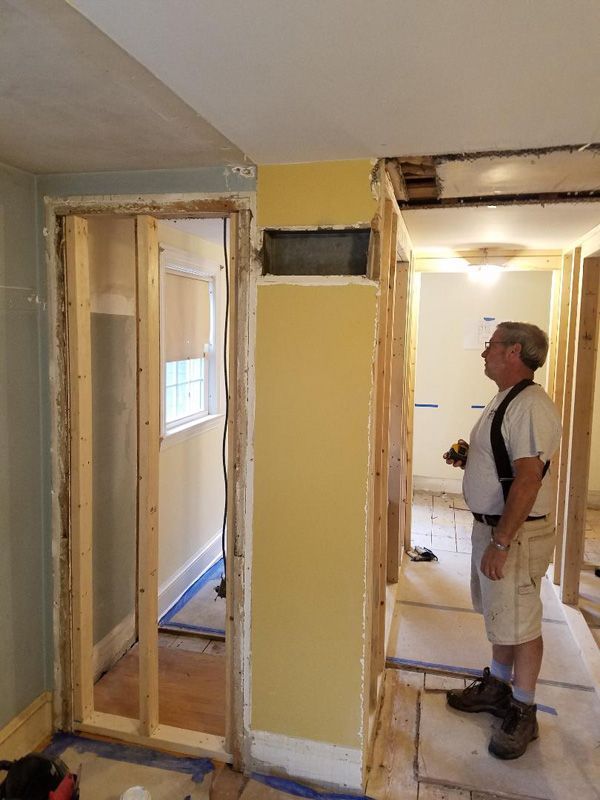 Partially remodeled room with exposed wall framing and a man inspecting the renovation